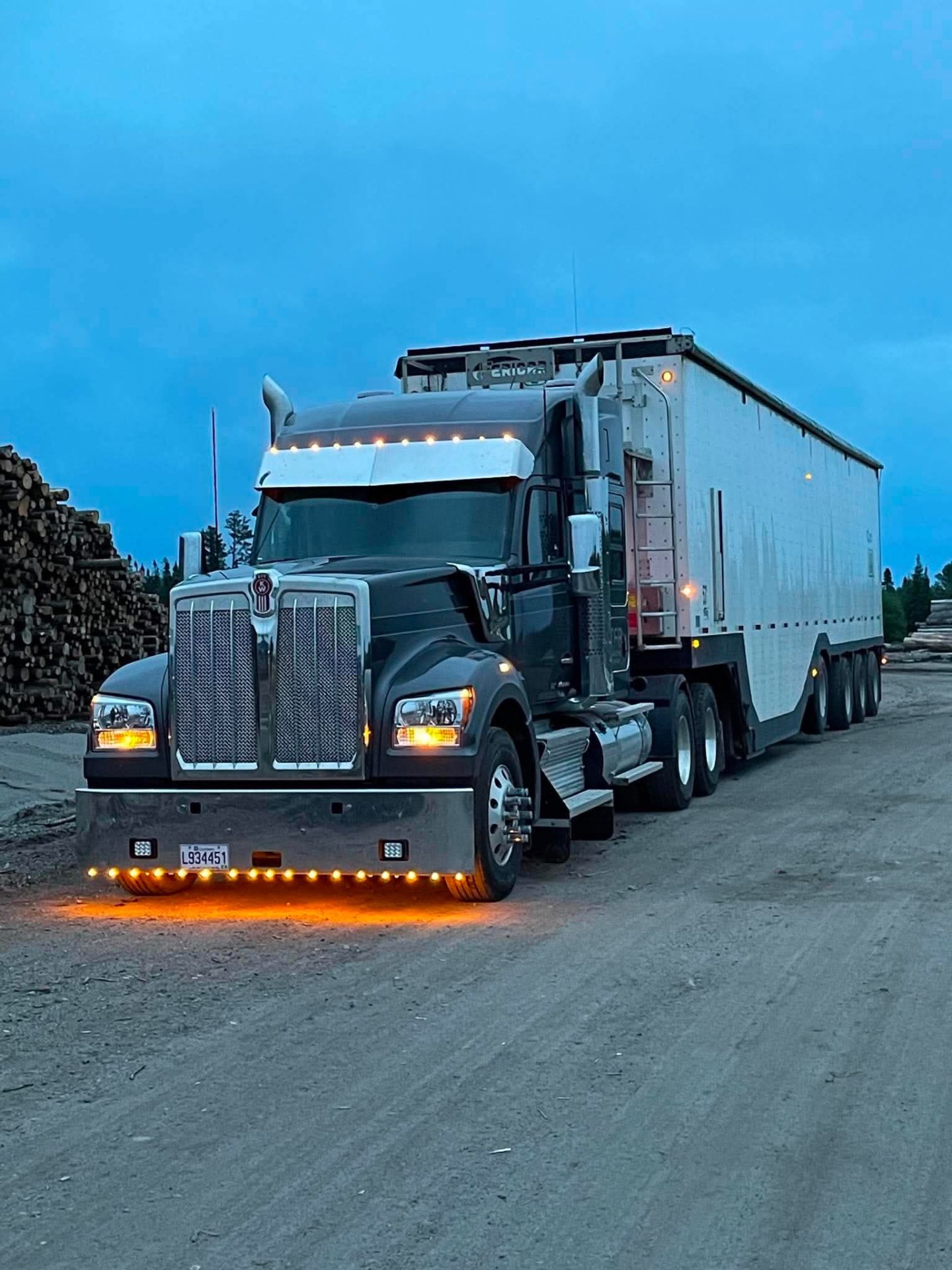 Kenworth noir TFB avec remorque à copeaux à la cour à bois au crépuscule