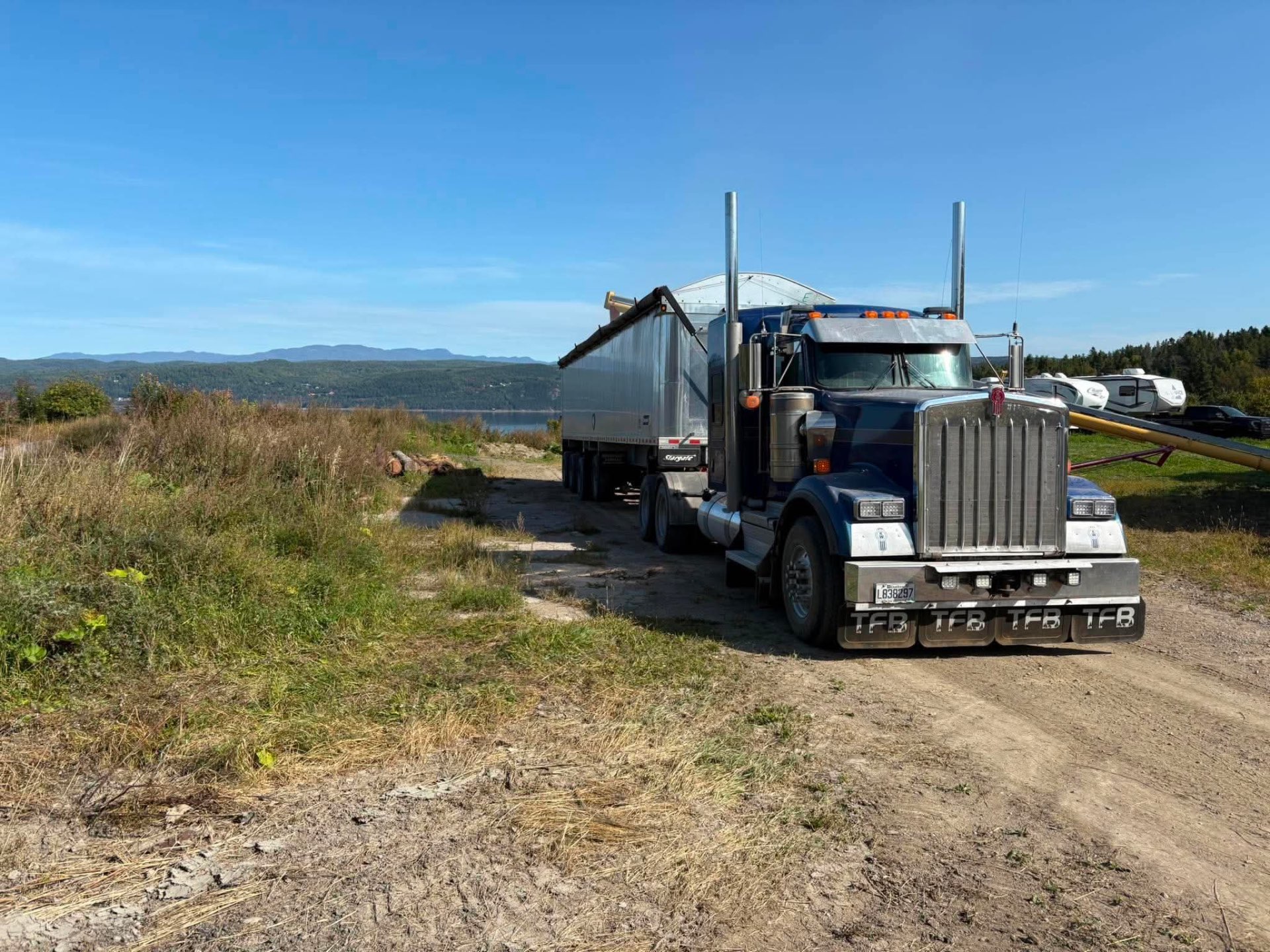 Kenworth bleu TFB tractant un trailer dompeur en aluminium devant le fjord du Saguenay