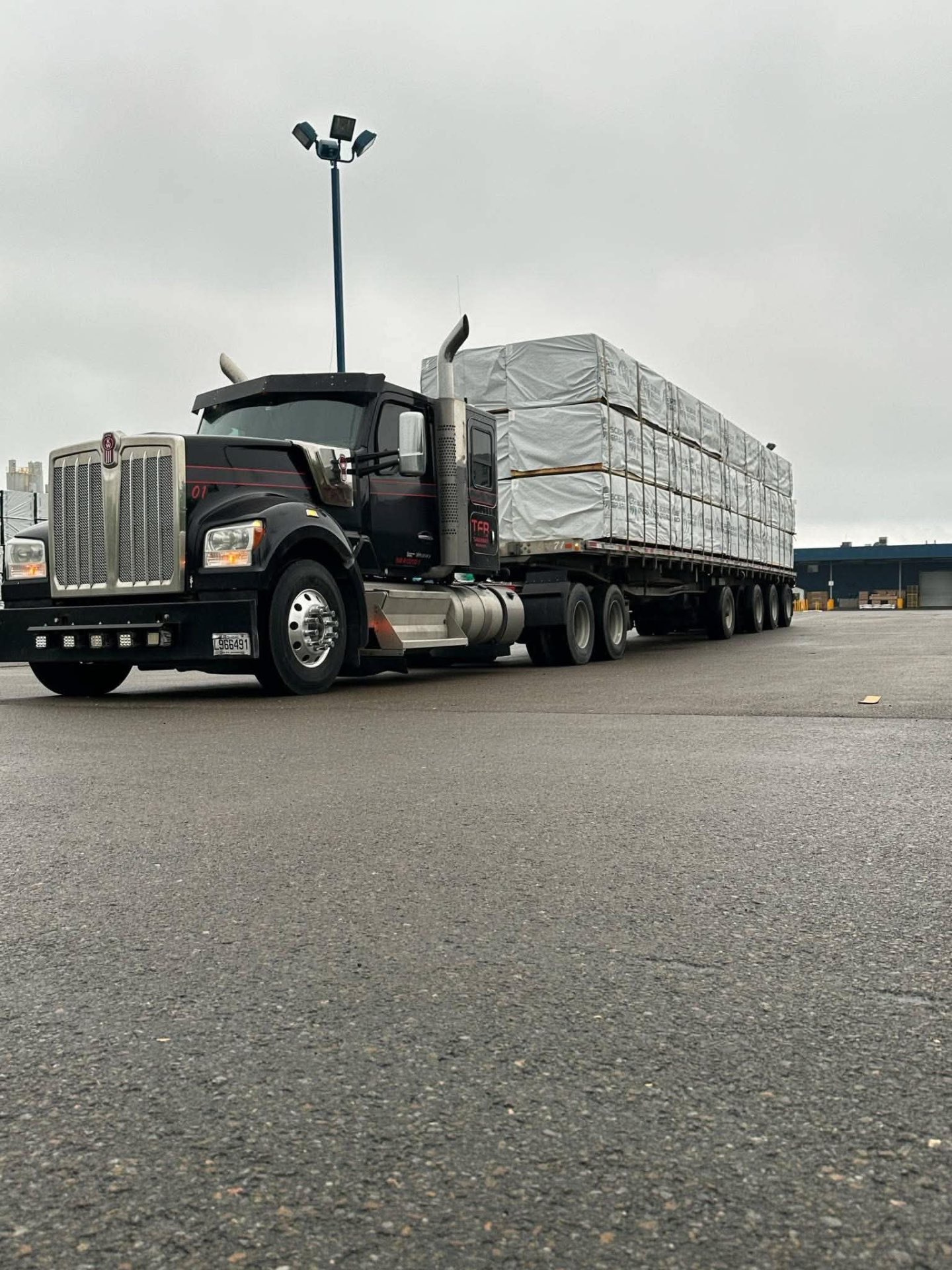 Kenworth noir TFB tractant un flatbed avec paquets de sciage emballés