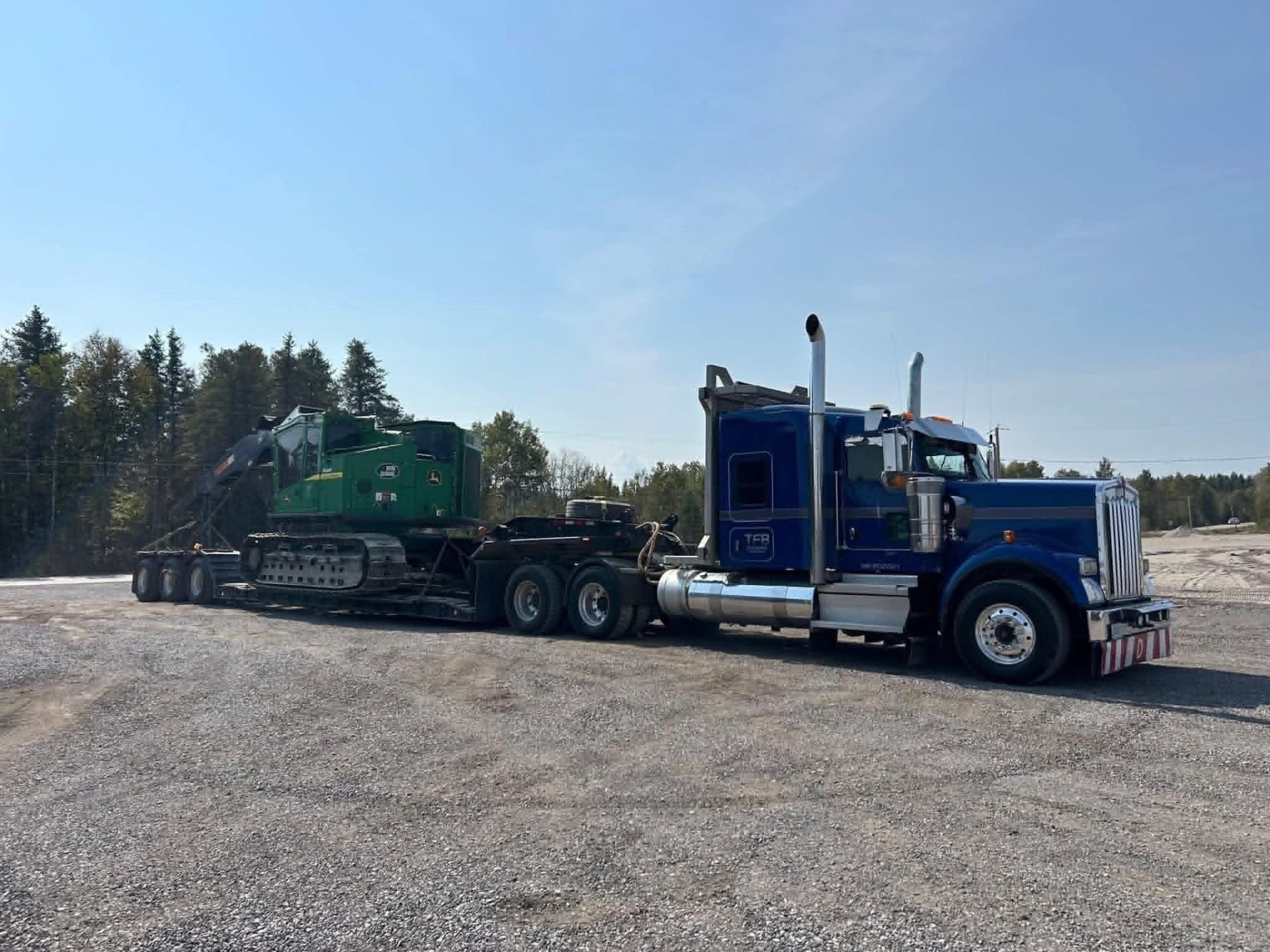 Kenworth bleu TFB tractant un fardier chargé d'une abatteuse John Deere